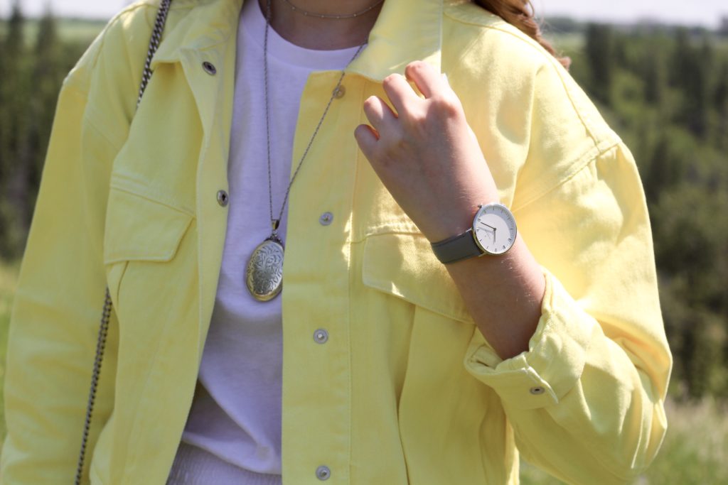 close up shot of grey leather watch and silver locket necklace